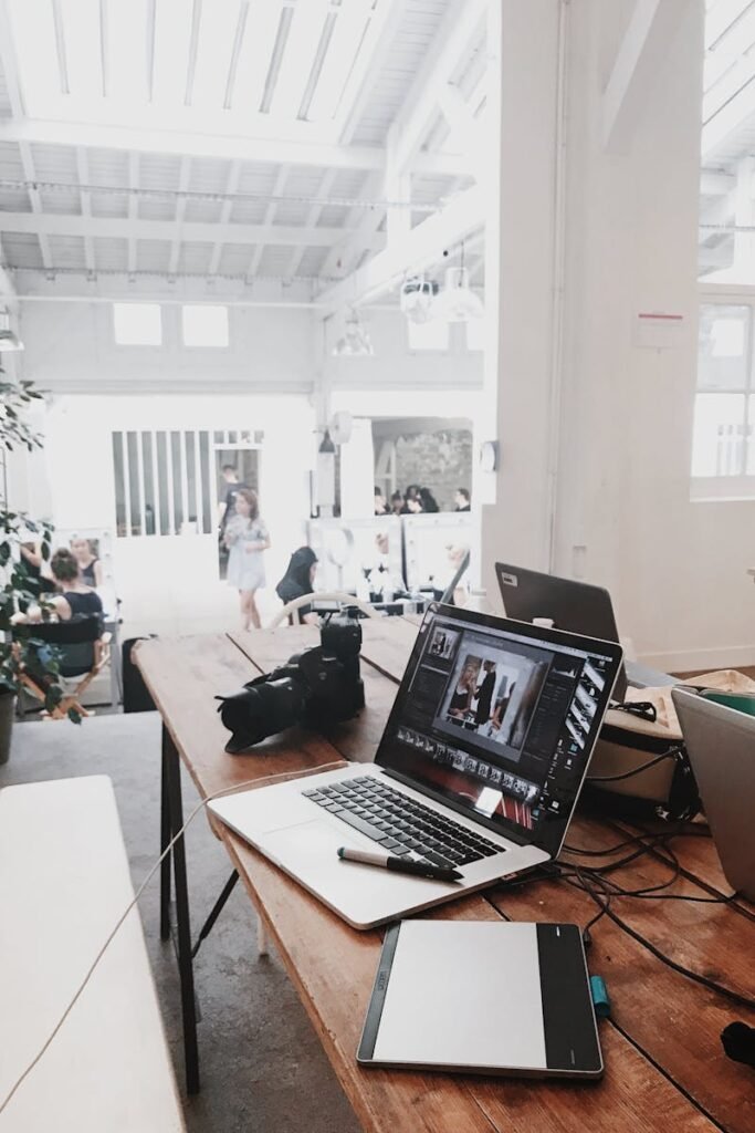 A bright, modern workspace featuring laptops, a camera, and a drawing tablet in an indoor office.